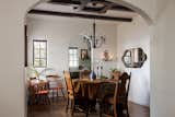 Dining room with round dining table and antique chairs, a black matte chandelier, seating in the corner, and exposed painted beams. A cut out looks into the kitchen and opens the space.  Photo 10 of 22 in Mission Tudor by Colossus Mfg.