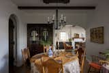 Dining room with round dining table and antique chairs, a black matte chandelier, seating in the corner, and exposed painted beams. The original built in vanity with stained glass windows leads into the living room.