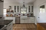 Kitchen with white shaker cabinetry, cream and brown backsplash tile, black matte hardware and faucet, open shelving, stain glass window upper cabinets, farmhouse sink, and lantern style lighting.