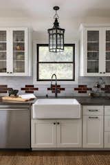 Kitchen with white shaker cabinetry, cream and brown backsplash tile, black matte hardware and faucet, stain glass window upper cabinets, farmhouse sink, and lantern style lighting.