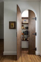 Custom built dark wood arched doors with antique metal hinges and handles leads to a built in pantry.
