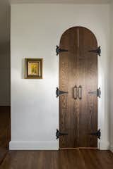 Custom built dark wood arched doors with antique metal hinges and handles leads to a built in pantry.