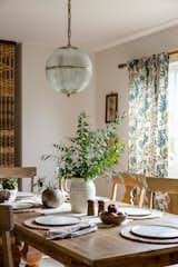 Dining room with light wood dining set, floral curtains, and aged brass sphere pendant light.