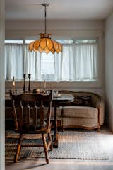 Breakfast nook with large reupholstered couch, antique wood table and chairs, and a stained glass vintage pendant light.