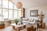 Southern California inspired living room with a neutral palate and natural materials through a grey cozy couch, woven rug, oversized wicker pendant, leather accent chairs, a custom light wood coffee table, and lots of natural lighting.