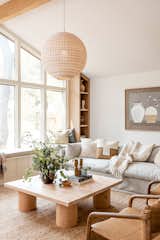 Southern California inspired living room with a neutral palate and natural materials through a grey cozy couch, woven rug, oversized wicker pendant, leather accent chairs, a custom light wood coffee table, and lots of natural lighting.
