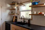 White Dal tiles are the backdrop in this kitchen for white washed open shelving, matte black hardware, and a woven vintage gold accented sink pendant.