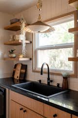 White Dal tiles are the backdrop in this kitchen for white washed open shelving, matte black hardware, and a woven vintage gold accented sink pendant.