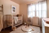 Peachy nursery room accented with a multi toned woven rug, refinished vintage cradle, and shear curtains.