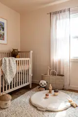 Peachy nursery room accented with a multi toned woven rug, refinished vintage cradle, and shear curtains.