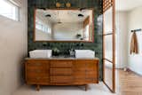 This antique dresser was given new purpose by implementing it as a bathroom vanity. Built into the wall, and custom tiled, this piece is the star against a green multi toned tiled bathroom wall with a flush mirror and black and gold sconces.