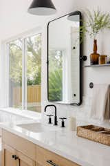 Ensuite bathroom with medium-light wood cabinetry, black matte hardware and appliances, white counter tops, and black matte metal mirror and pendant.