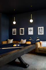 Game room with stained cement floor, dark blue moody walls, and furnished with dark wood/blue felt pool table, twin leather couches, and cement milk globe pendant lighting.