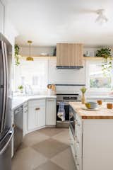 Dual toned checkered floor, pops of blue tile, and yellow accent lighting bring a bright harmony to this kitchen with a butcher block free standing island, clean white cabinetry and quartz countertops.