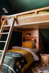 A cabin isn't complete without bunk beds. These custom built beds with book nooks, boast fun patterns and bright colors through its bedding, green sconces, and dark green walls.