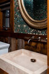 Powder room with antique mirror, floral wallpaper, stone vessel sink, reclaimed wood paneled walls, and wall mounted faucet with gold finish.