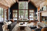 This living rooms A-frame wood paneled ceiling allows lots of natural light to shine through onto its Farrow & Ball dark shiplap walls and iron covered fireplace. The space boasts a large geometric rug made of natural fibers from Meadow Blu, a dark grey heather sofa from RH, a custom green Nickey Kehoe couch, a classic Eames chair, a McGee and Co. gold chandelier, and a hand made reclaimed wood coffee table.