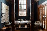 Farrow & Ball painted black paneled dining room with wrapped beams, french doors, paneled wood ceiling, a large dining table for eight, a mountain themed tapestry, and Anders pendant lighting.