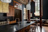 Rustic industrial kitchen with textured dark wood cabinetry, black countertops and backsplash, an iron wrapped hood, and milk globe sconces lead into the dining room that boasts a table for 8, wrapped beams, oversized wall tapestry, and an Anders pendant.