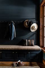 Moody mudroom with Farrow & Ball painted black shiplap walls, built in pegs for coats, and a custom made bench with hidden storage and gold hardware.