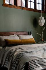 Ensuite bedroom gives out calming nature vibes through its green walls, midcentury furniture, layers of Parachute bedding, and geometric pendant lighting.
