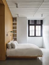 The bedroom is minimalist with built-in shelves. The walls are white Oak and white painted bricks. The custom bed is white oak.