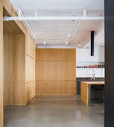 View to the kitchen, the reclaimed wooden island and the stainless steel counter. The white oak cabinetry, the floor is polished concrete. The ceiling is white with exposed mechanical ducts.
