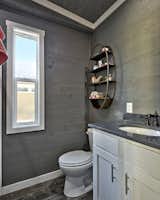 Bath Room, Two Piece Toilet, Full Shower, and Medium Hardwood Floor In tiny bathrooms with a simple and modern aesthetic, adding a decorative yet functional shelf adds a touch of elegance to a room. The bathroom in this industrial tiny home in Texas has a metal shelf with a brass finish, giving a touch of warm color to this gray and white bathroom.  Photo 5 of 15 in 15 Tiny Bathroom Ideas For a Beautiful and Functional Space from The Haven: Tiny Home in East Austin