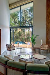 A sculptural installation of refurbished teak-wood panels along the double-height main wall adds warmth and colour.  The otherwise minimalist room is defined by generously high ceilings and a breath-taking view of the infinity pool and the home’s sprawling gardens. Customised modular furniture in teak wood and muted accents face the accordion glass doors leading outside. 