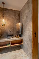 A guest powder room showcases a uniquely stylised interior. Concrete walls and floors give the space a monolithic appearance. Subdued lighting and clean lines balance an industrial, yet minimalist, use of metal, stone, glass and wood. 