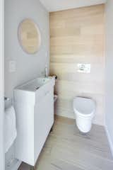 Main floor power room with wall mounted toilet and white oak flooring that has been carried up the back wall.
