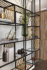 The texture of the perforated brass is repeated in the floating library, which is a composition of layered shelving, which appears as thin, floating shelves providing an overall result that is elegant,  light and airy.