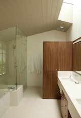 The master bathroom features a vaulted ceiling in stained douglas fir, a freestanding walnut cabinet that doubles as a privacy divider for the toilet, a limestone counter that  integrates with the tall cabinet, a limestone floor, and a steam shower.