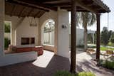 The details of this outdoor but covered room integrate the exterior and interior details.
The flooring and roof match the pergola, and the massive walls and fireplace, along with the custom historic iron chandelier, make it feel like a room. The arched opening frames views of the Santa Monica mountains.