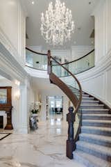 The open-concept french-style estate includes iconic features such as a custom curved glass staircase with unique walnut railings, handcrafted furnishings and extravagant ceiling details throughout.