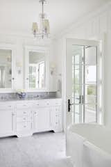 Old Grove estate master bathroom featuring free standing tub, door out to the master porch, custom built-in vanity and medicine cabinets with 3 light chandelier.