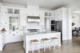 Old Grove estate kitchen featuring stainless steel appliances, antique hardware, glass display cabinets, hidden storage, window looking into internal staircase with hurricane proof glass. On the other side of the kitchen is a dining area overlooking Spanish moss.