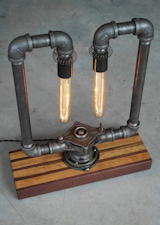 The Pipe Threader Edison Lamp .  The centerpiece of this lamp is an early to mid 1900’s pipe threader we upcycled from an estate sale of an amazing guy who was a jack-of-all-trades after serving his country in WW2 as a B25 gunner.

This light, assembled with various plumbing pipe fittings, some old and some new, will bring out the nostalgia of a time gone by.  Looks gorgeous in any home, loft, business, office, lounge, restaurant or anywhere with Industrial machine-age décor inspiration.  

To purchase:
https://toddalanwoodcraft.com/collections/lighting/products/the-pipe-threader-edison-lamp

Dual steel pipe arms extend out the pipe threader and support reproduction vintage sockets that hold two incandescent Edison bulbs.  The pipe threader is secured mounted to the beautiful Walnut and Maple board we created specifically for this lamp, from cut-offs of our serving boards, creating no wood waste.

We’ve added small accents like a decorative springs also purchased at the estate sale, and the lamp features a top mounted captains wheel style dimmer switch for easy lighting control.

This light comes with a black braided industrial era reproduction cloth cord and reproduction antique plug. Lights come featured with inset low profile non-skid feet attached to the bottom.