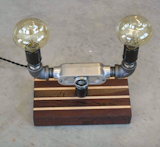 Dual Lantern Lamp on Custom Roasted Oak and Pacific Maple Base. 
This beautiful vintage inspired industrial Chic lamp reminiscent of old factory light fixtures features a steel pipe double lamp structure that has 2 Lantern style Edison bulbs (Included with purchase). A large dimmable dial knob centered on the metal adds to the uniqueness of this light.

To purchase:
https://toddalanwoodcraft.com/collections/lighting/products/duel-lantern-lamp-on-custom-roasted-oak-and-pacific-maple-base

The rich dark and blonde wood base is made from Roasted Oak and Pacific Maple. All of our wood bases are created by utilizing the high quality castoff pieces from the production of our cutting, charcuterie and serving boards, so we have no more than two percent waste.  