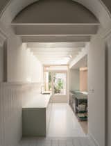 Occupants step down into the kitchen from the dining room. A run of cabinets with an integrated sink directly abuts the threshold between the rooms, where an original plaster archway also meets new ceiling joists.