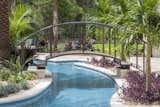 Outdoor, Raised Planters, Grass, Back Yard, Trees, Shrubs, Hardscapes, and Walkways A bridge connects the grotto island with the travertine patio adjacent to the home's game room.   Photo 9 of 10 in Ballmont Lazy River Chase by Laurie Rudd