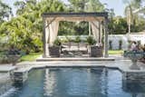 Ryan Hughes’s custom designed pergola softly shades guests with an elegantly flowing performance fabric and encourages relaxation around the custom designed fire pit coffee table, surrounded by Patio Renaissance furnishings. This custom design thoughtfully includes multiple conversation areas offering both privacy as needed and conviviality across the space. 
