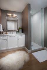 A plush rug extends the cozy theme within the guest bathroom positioned in front of the vanity and walk in shower. 