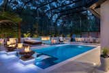 Fire lights the space from pots to a wall feature in this indoor-outdoor living area. Glistening off the calm waters of the modern multi-level pool, the light offers a welcoming invitation to calm and relaxation. 