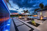 Glistening water streams on aria wall of oceanside tiles through the use of outdoor lighting and incorporating a water feature by Great American Waterfall Company. The swim up bar lounge is bordered by stepping pavers and landscaping with FX Lighting.