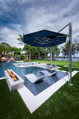 A cooling cantilever TUUCI umbrella offers shade over the sun shelf in the pool. Ledge Loungers and a custom fire feature create an attractive lounging area in the outdoor space. 