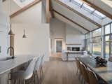 The interior is illuminated by natural light streaming through a skylight that runs through the house, creating a striking interplay of light and shadow. Exposed wooden beams and lime-washed walls enhance the organic feel of the space, while the large windows offer expansive views of the surrounding landscape, blurring the lines between indoors and outdoors.