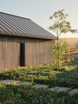 Part of the house is partially hidden within a naturally rugged landscape, shrouded in mist and bathed in soft sunlight. A natural stone path winds through the terrain, leading toward the garage, further emphasizing the home's seamless connection to its surroundings.