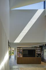 A bespoke timber joinery unit serves as a semi-partition between the kitchen and the living space, giving a sense of separation without disconnection. Dramatic patterns of light and shadow from the sculptural skylight play over the space.