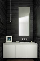 The dark tiled walls of the bathroom strike contrast with the stark white vanity unit.
